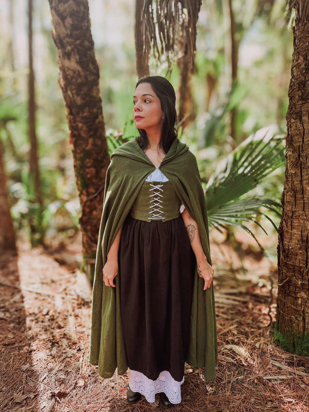 Woman in a green cloak and dark dress standing in a forest